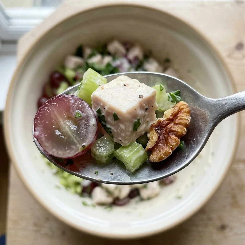 Close-up spoonful showing the chunky, creamy texture of chicken salad with grape and pecan.