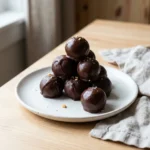 Glossy chocolate peanut butter balls stacked on a white plate as an easy no-bake dessert