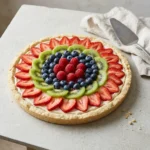 Overhead view of a finished fruit pizza with strawberry slices, kiwi, blueberries, and raspberries arranged in bright bands