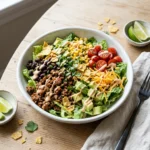 Bowl of easy taco salad with seasoned ground beef, romaine, avocado, and crushed tortilla chips on a wooden table
