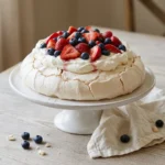 Whole berry pavlova with whipped cream and strawberries on a white cake stand